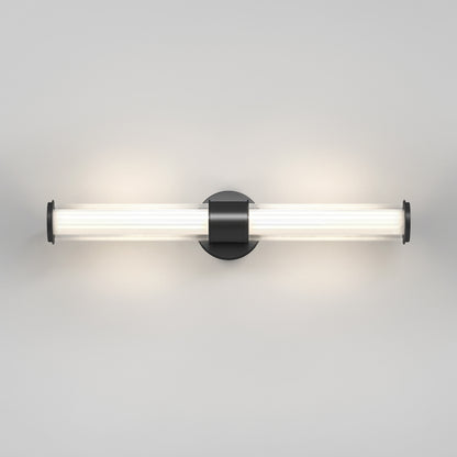 The Artika Kendra LED contemporary bathroom vanity light features a central black circular base and a horizontal frosted glass tube, emitting soft white light against a plain light gray wall.