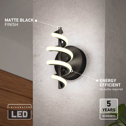The Artika Chorus LED Wall Light, featuring a spiral LED design and matte black finish, is mounted on a gray wall. Labels highlight its energy efficiency, integrated LEDs, 5-year warranty, and no need for bulbs.