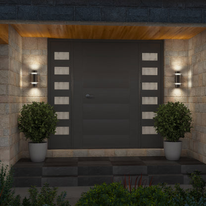 A modern front door with horizontal panels and rectangular glass inserts on each side, flanked by two potted shrubs and illuminated by a pair of Artika D4 indoor-outdoor wall lights mounted on a stone wall.