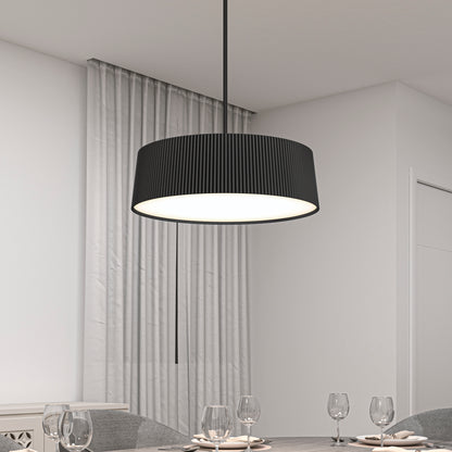 The Artika Groove Drum LED contemporary pendant light in black, featuring a ribbed texture and 3 CCT settings, hangs above a minimalist dining table set with glasses in a white room with sheer curtains.