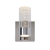 A modern wall sconce with a chrome base and a cylindrical glass shade containing small bubbles, emitting light from its base.