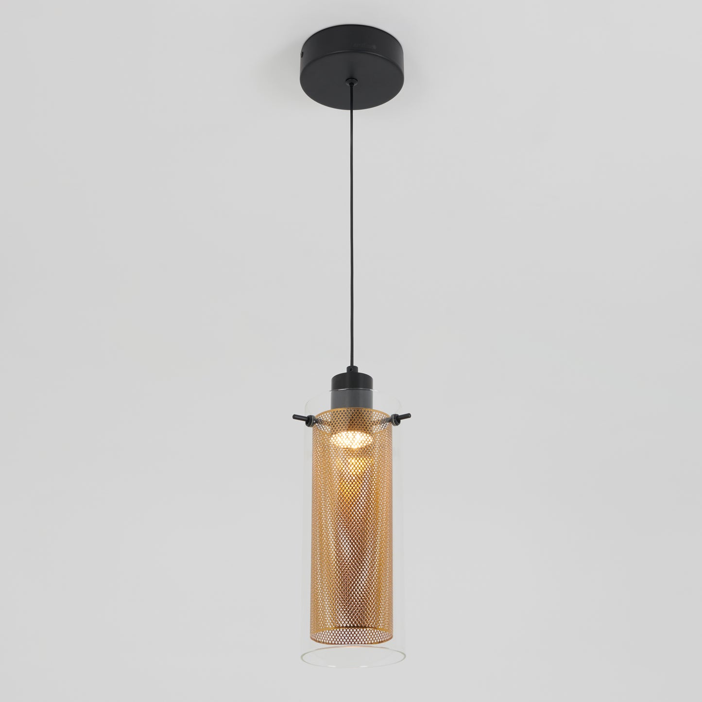 The Artika Oxion 1-light LED pendant features a black ceiling mount and cord, with a cylindrical glass shade and perforated gold metal inner layer, shown illuminated against a plain white background.