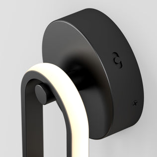 Close-up of the Artika Catena modern LED wall sconce 5 CCT, a black wall-mounted fixture featuring a curved illuminated LED strip and circular base, shown against a plain light gray background.