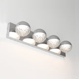 A modern wall light fixture with four spherical glass shades mounted on a rectangular metallic base, emitting bright white light against a plain light-colored wall.