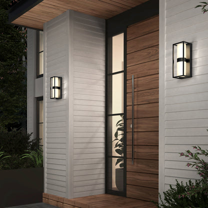 Modern house entrance features a vertical wood panel door, tall glass window, and Artika Sherman modern LED indoor-outdoor wall lights (5 CCT) on light gray siding. Contemporary black and white sconces and some plants are visible near the doorway.