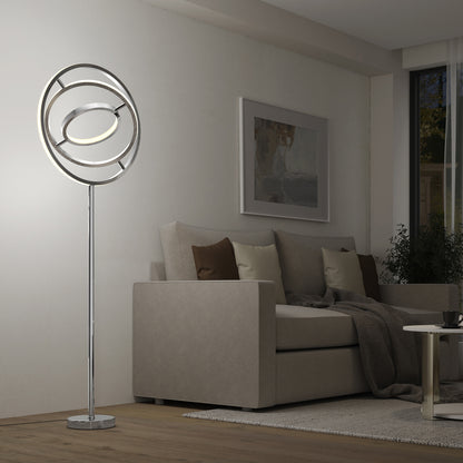 A modern living room featuring a beige sofa, brown and cream cushions, a dark throw, and the Artika Pivot modern LED floor lamp (3 CCT) with circular rings, set beside a coffee table and wall art.