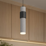 A modern cylindrical pendant light with a concrete texture and black accent hangs from the ceiling in front of light wood cabinets in a contemporary interior setting.