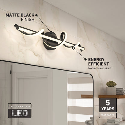 The Artika Coda modern LED bathroom vanity light 5 CCT in matte black is mounted above a bathroom mirror on a tiled wall, showcasing its integrated LED, energy efficiency, and five-year warranty. A shelf with towels and a plant is nearby.