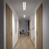 A well-lit hallway with light wood floors and doors on both sides, leading to a bright living area with a plant and sheer curtains at the end.