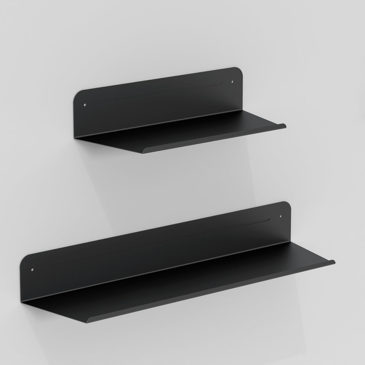 Two black metal floating shelves are mounted on a plain white wall, one above the other, with the upper shelf being smaller than the lower one. Both shelves have a minimalist, modern design.