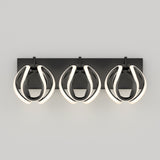 A modern wall sconce with three oval-shaped, black light fixtures each framed by curved, glowing white LED strips, mounted on a rectangular black base against a plain gray background.