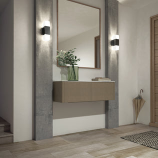 A modern entryway showcases a floating cabinet, large mirror, green vase with branches, umbrella stand, textured rug on light wood floor, and Artika's Lennox indoor-outdoor LED wall light 3 CCT in matte black for adjustable white lighting.