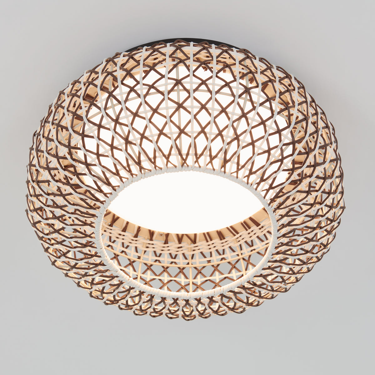 A round ceiling light with a woven rattan or wicker lampshade, featuring an open lattice pattern, glowing softly against a plain white ceiling.