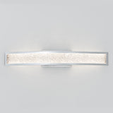 A modern wall sconce with a curved, rectangular chrome frame and a textured, frosted glass diffuser emits a soft, even light against a plain white background.