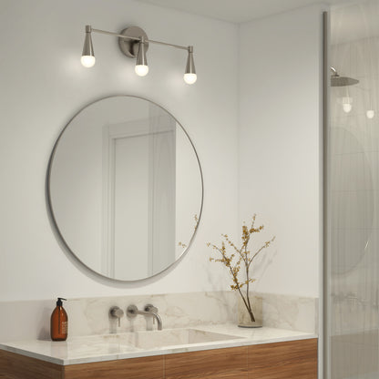 A modern bathroom features a round mirror above a marble countertop, wall-mounted faucet, soap dispenser, vase with branches, and the Artika Wayden LED mid-century vanity light (3 CCT) above the mirror. A glass-door shower appears on the right.