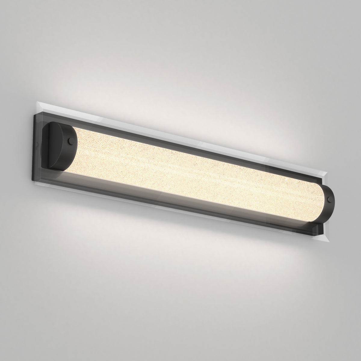 A modern wall-mounted light fixture with a long, cylindrical frosted glass shade and black end caps, emitting a soft, warm glow against a light gray wall.
