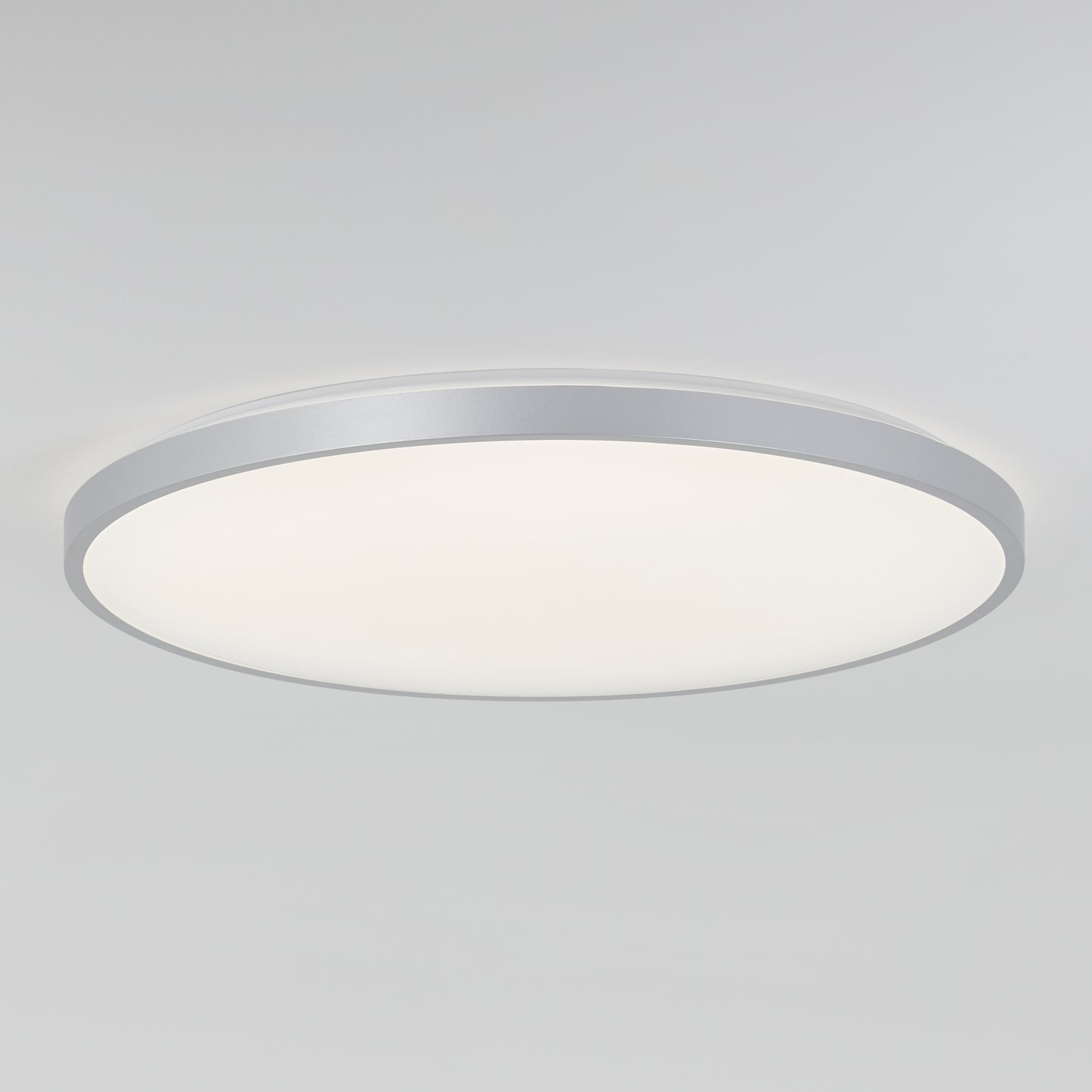 The Artika Jupiter 23 in. LED flush mount light features a modern round design with a white diffused cover and silver rim, mounted on a plain white ceiling. Includes remote control.