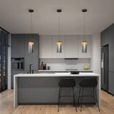 Modern kitchen with a large island, two black chairs, pendant lights above, gray and white cabinets, built-in appliances, and wood flooring. The space is minimalistic and well-lit with a sleek, contemporary design.