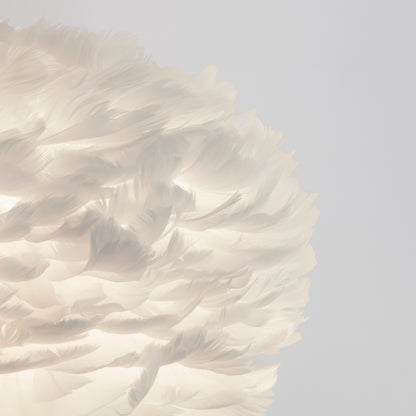 Close-up of the Artika Plume LED pendant light, featuring a white feather lampshade that glows softly against a plain light gray background, highlighting its fluffy and delicate texture.