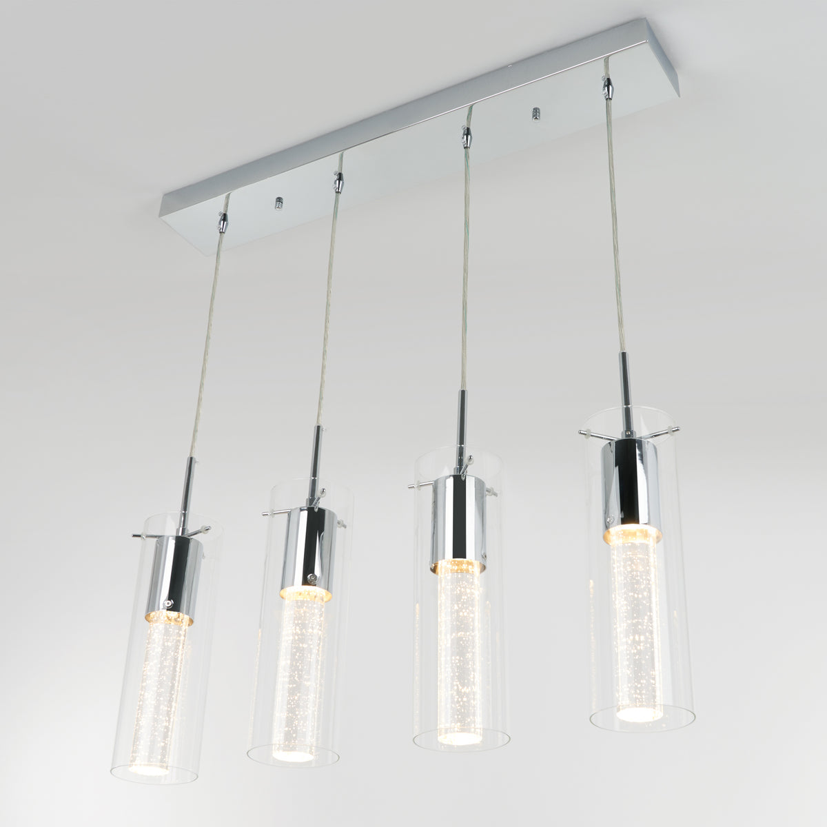 Modern rectangular ceiling light fixture with four hanging pendant lights, each featuring a cylindrical glass shade and chrome accents, suspended by thin cables, illuminated against a plain white background.