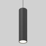 A modern, cylindrical black pendant light with vertical grooves hangs from the ceiling against a plain gray background. The bottom of the light is open, emitting a soft white glow.