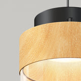 A close-up of a modern pendant light featuring a light wood grain outer shade, a black metal fixture above, and a glowing bulb underneath, set against a plain gray background.