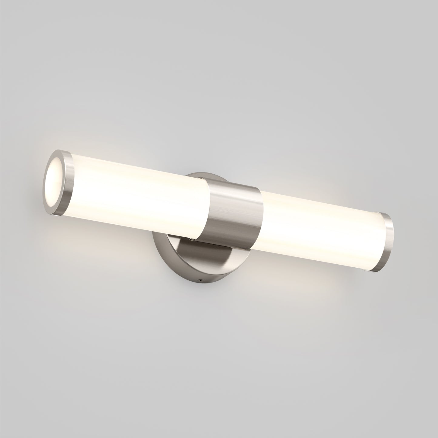 The Artika Adina modern bathroom vanity light 3 CCT is a wall-mounted LED fixture with a brushed metal base and cylindrical frosted glass shade, casting soft white light against a light gray wall.