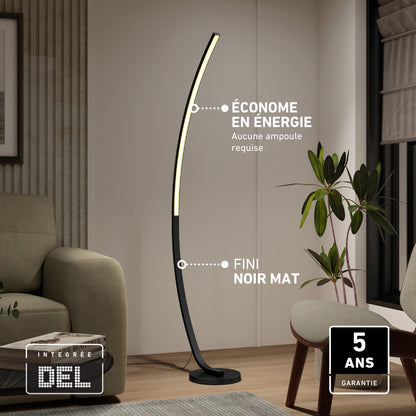 The Artika Arc LED Floor Lamp, featuring a matte black finish, stands beside a green armchair and potted plant. This modern, dimmable lamp saves energy, needs no bulb, and includes a 5-year warranty.