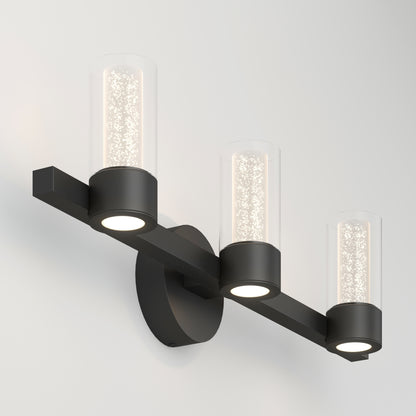 The Artika Novello modern LED bathroom vanity light features three cylindrical glass shades with bubble details, mounted on a matte black horizontal bar for a sleek, contemporary look.