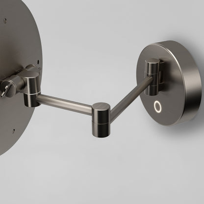 A close-up of the Artika Radia Cordless LED Cosmetic Mirror shows its modern, wall-mounted adjustable metal arm with circular wall plates and a brushed finish against a light gray background.
