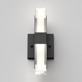 A modern black wall sconce with a rectangular base and horizontal frosted glass shade emitting soft white light, mounted on a plain light gray wall.