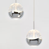 Two modern spherical pendant lights with a metallic silver lower half and translucent upper half, speckled with small white dots, hang against a plain white background.