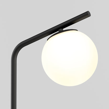 The Artika Clayton dimmable LED modern mid-century floor lamp features a matte black curved stand and a round frosted white glass shade, softly glowing against a plain light gray background.