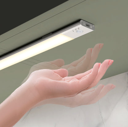 A hand activates the Artika Outline under cabinet LED light 3CCT, a slim, rectangular motion-sensor fixture installed beneath a green cabinet, demonstrating its touchless operation.