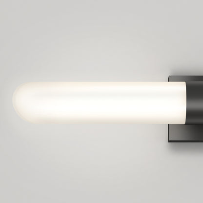 The Artika Wilton LED modern bathroom vanity light 5 CCT features a frosted glass cylinder shade on a sleek black square base, casting a soft, diffused white glow against a light gray wall.