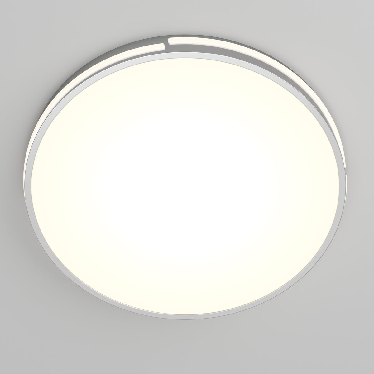 A round, modern ceiling light fixture emitting a bright, even white glow, mounted on a plain light gray ceiling. The fixture has a simple, minimalistic design with a thin metallic rim.