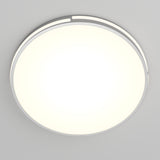 A round, modern ceiling light fixture emitting a bright, even white glow, mounted on a plain light gray ceiling. The fixture has a simple, minimalistic design with a thin metallic rim.