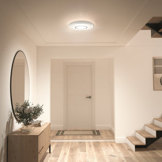 A modern hallway with wood floors, a round mirror, console table, plant, and Artika Horizon 13 in. LED flush mount ceiling light.