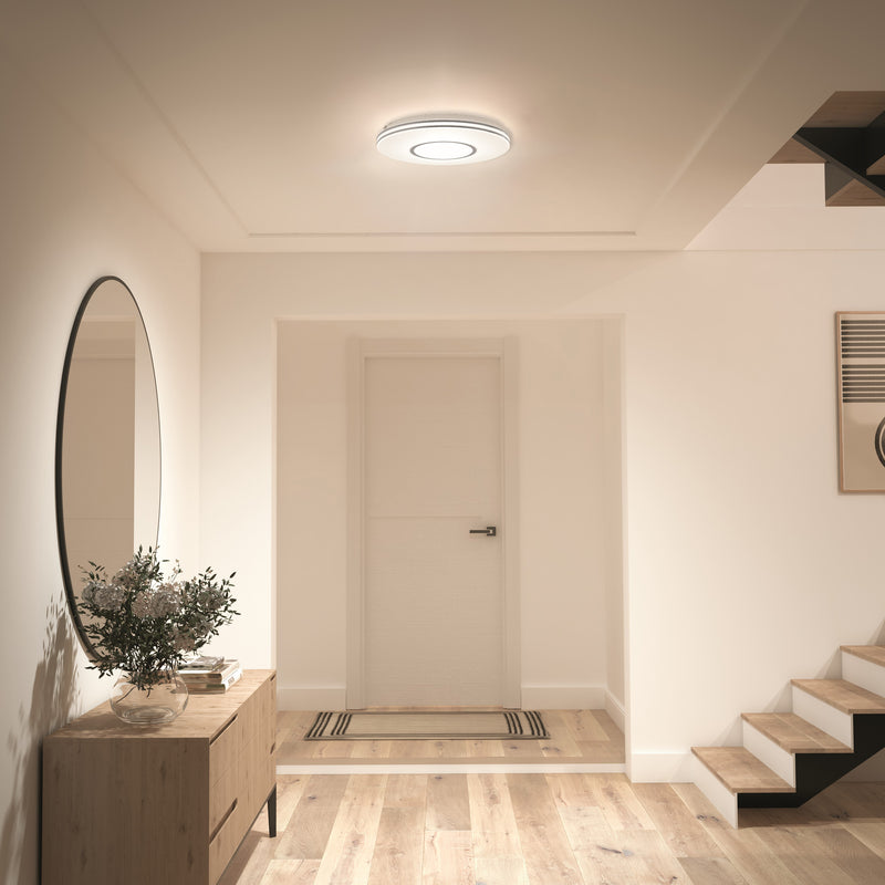 A modern hallway with wood floors, a round mirror, console table, plant, and Artika Horizon 13 in. LED flush mount ceiling light.