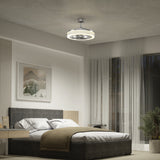 A modern bedroom with a gray upholstered bed, neutral bedding, a nightstand, large window with sheer curtains, a potted plant, wall art, and a contemporary ceiling fan with integrated lighting.