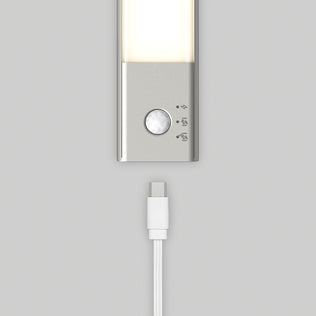 A close-up of the Artika Outline under cabinet LED light 3CCT, featuring a motion sensor and three icons, sits above a white USB-C charging cable on a light gray background.