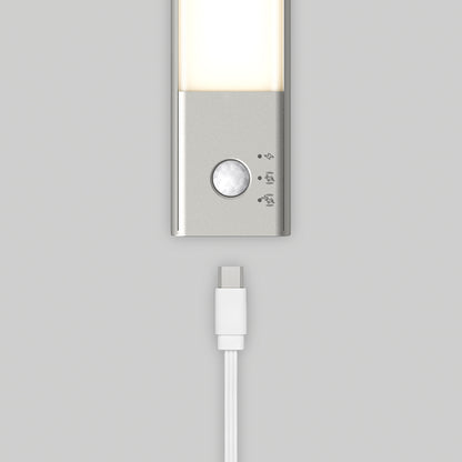 A close-up of the Artika Outline under cabinet LED light 3CCT, featuring a motion sensor and three icons, sits above a white USB-C charging cable on a light gray background.