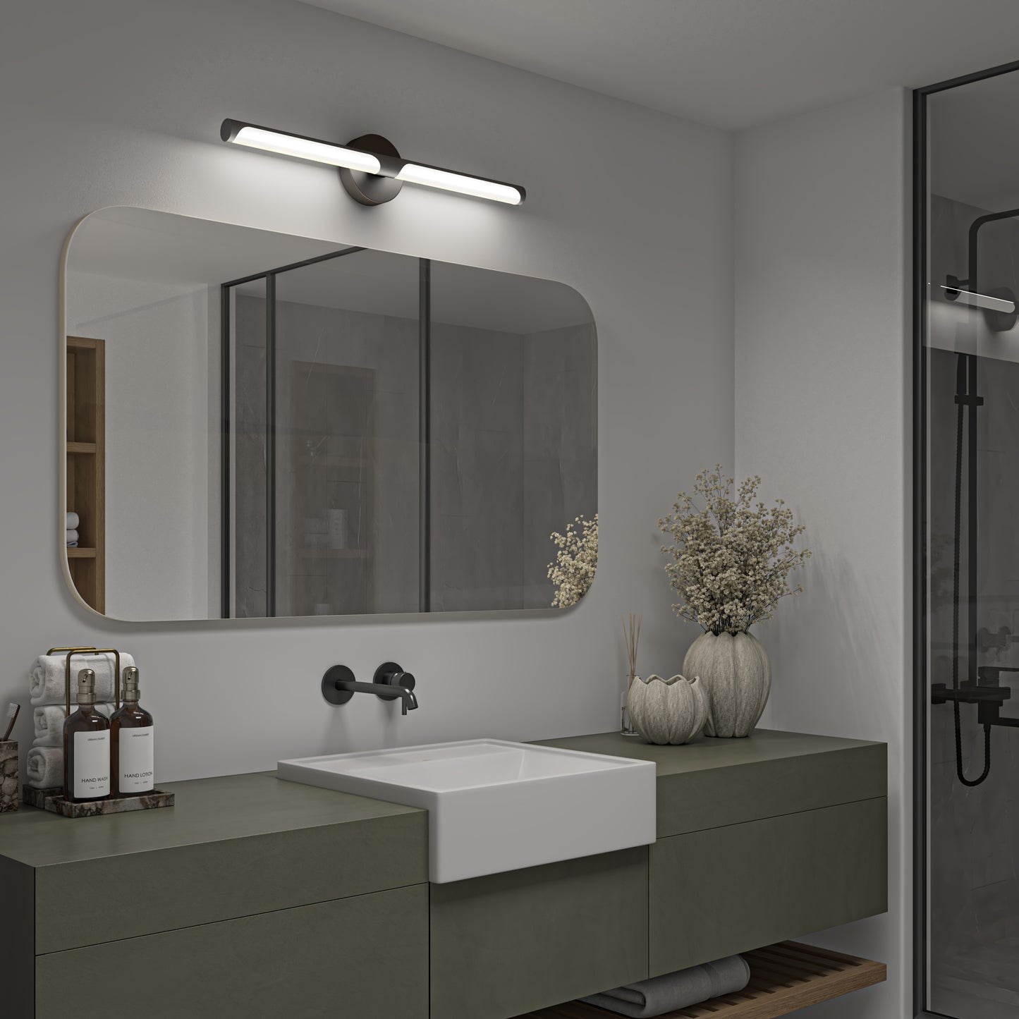 Modern bathroom with a rectangular mirror, Artika Ilona LED vanity light 5 CCT black above, white sink, green vanity, decorative vases with dried flowers, toiletries, and glass shower enclosure in the background.