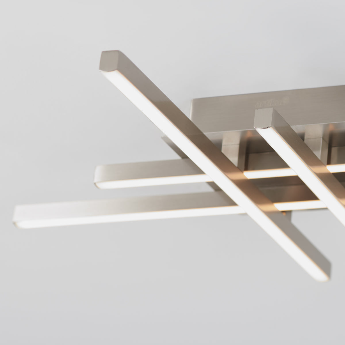 Close-up of a modern ceiling light fixture with four horizontal, rectangular LED light bars in a brushed metal finish, arranged in a staggered, geometric pattern against a plain white ceiling.