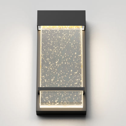 The Skyler indoor-outdoor LED wall light by Artika features a modern rectangular design with a clear panel of embedded air bubbles, illuminated warmly from the top and sides.