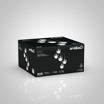 A black box displays the Artika Oracle modern 5-light LED pendant, featuring five hanging glass lights on the packaging with product details on the sides, set against a white gradient background.