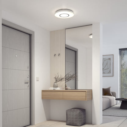 A bright, modern entryway features a light gray door, floating wooden console with two drawers, large wall mirror, decorative branches in a vase, pouf, and is illuminated by the Artika Horizon 13 in. LED flush mount light with 3 CCT.