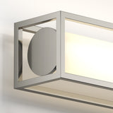 A modern wall-mounted light fixture with a brushed metal frame, featuring a geometric design with a circular accent and a frosted panel emitting a soft glow.