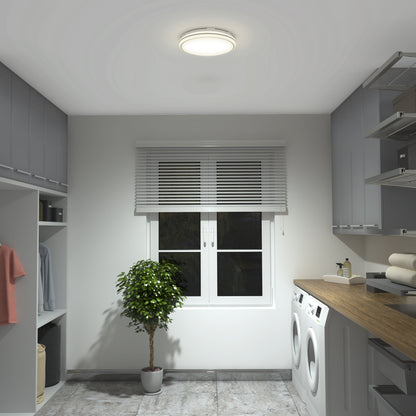 A modern laundry room with gray cabinets, a countertop holding folded towels, washer and dryer, potted plant, and a window with white blinds is lit by the Artika Emina 13 in. LED flush mount light 3 CCT.