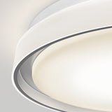Close-up of a modern, circular ceiling light fixture with layered, smooth white and metallic elements, emitting a soft, diffused glow against a light gray background.